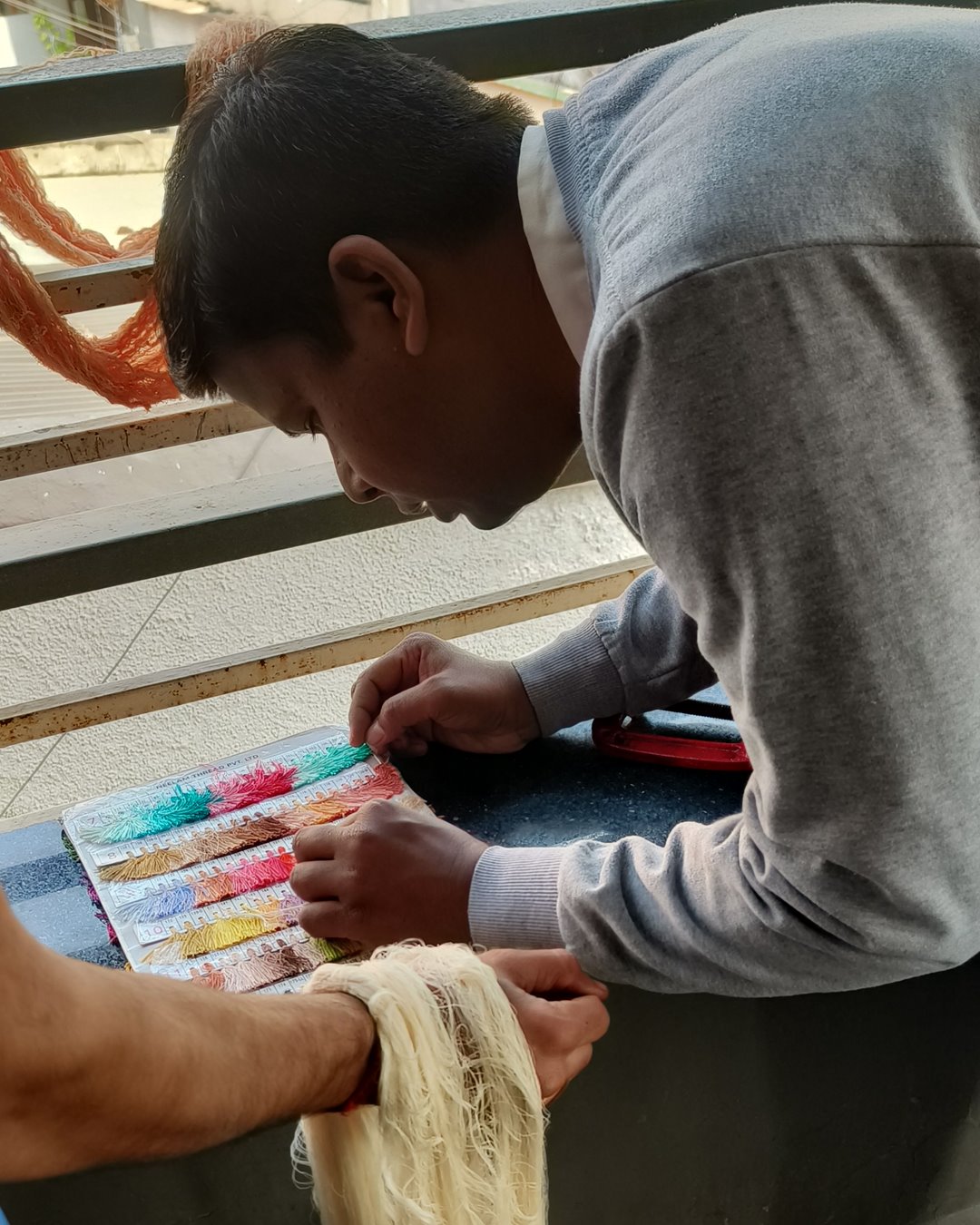 A dyer leaning over a shade card, matching thread colours while a hank of raw yarn is held beside it