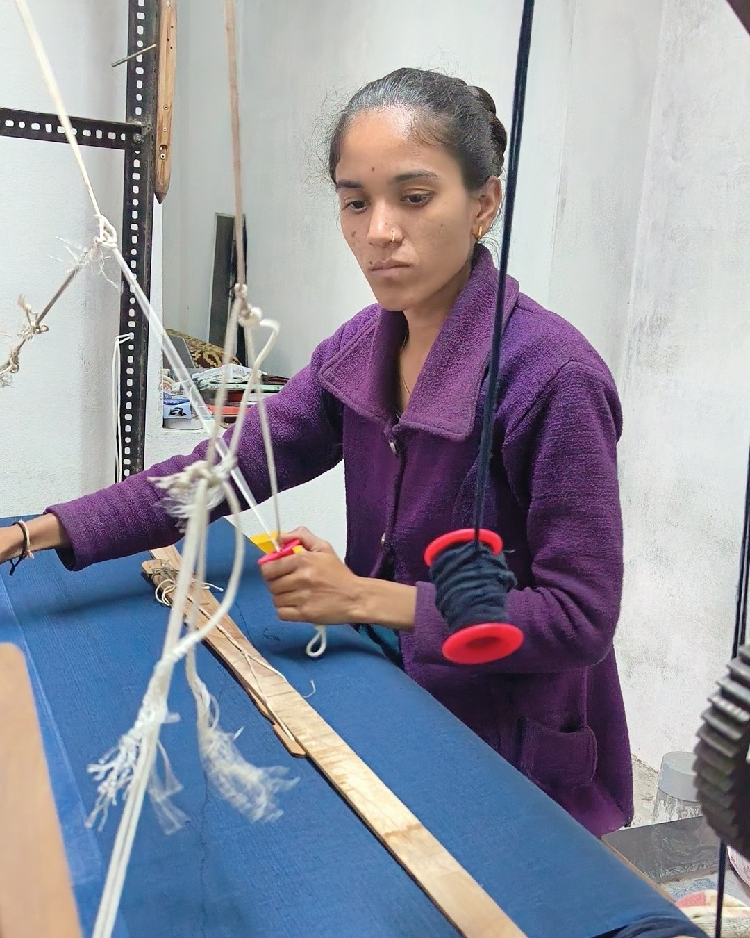 A young weaver passing an indigo weft bobbin across blue cloth on the loom